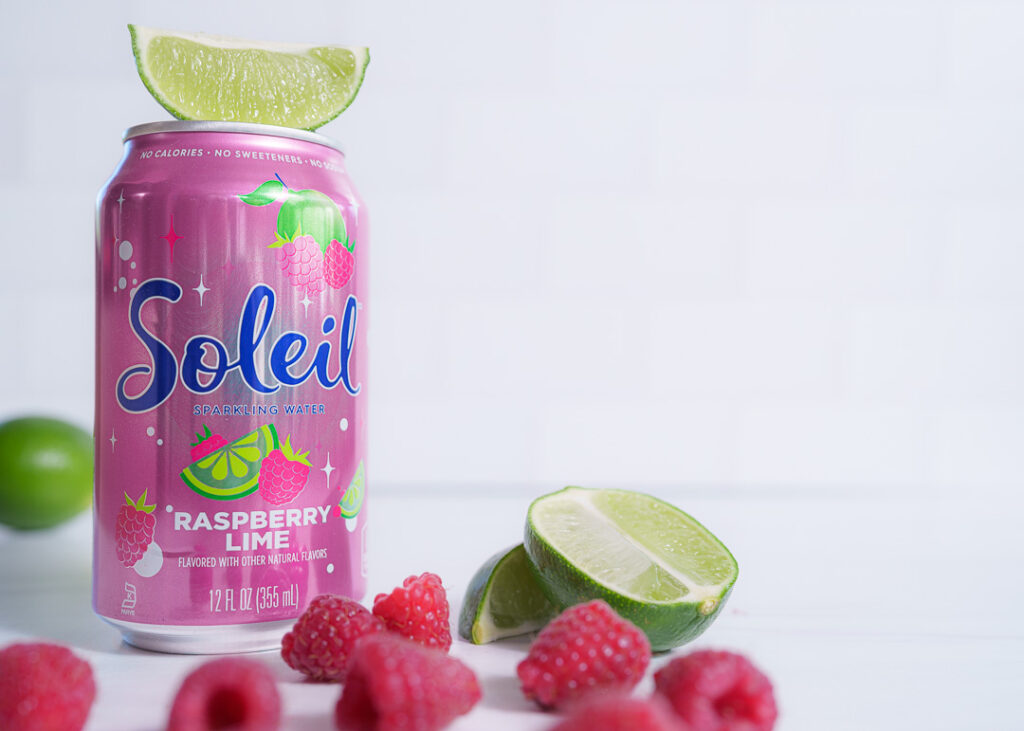 7 Ways a Brand Photoshoot Can Save You Time Creating Social Media Content 4 Pink can of Raspberry Lime Soleil with cut limes and raspberries on white background with negative space on the right side.