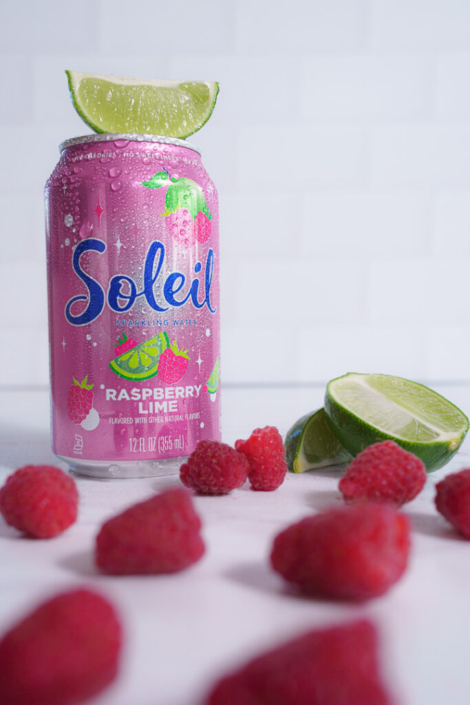 7 Ways a Brand Photoshoot Can Save You Time Creating Social Media Content 1 Pink can of Raspberry Lime Soleil with cut lime and whole raspberries on white background.