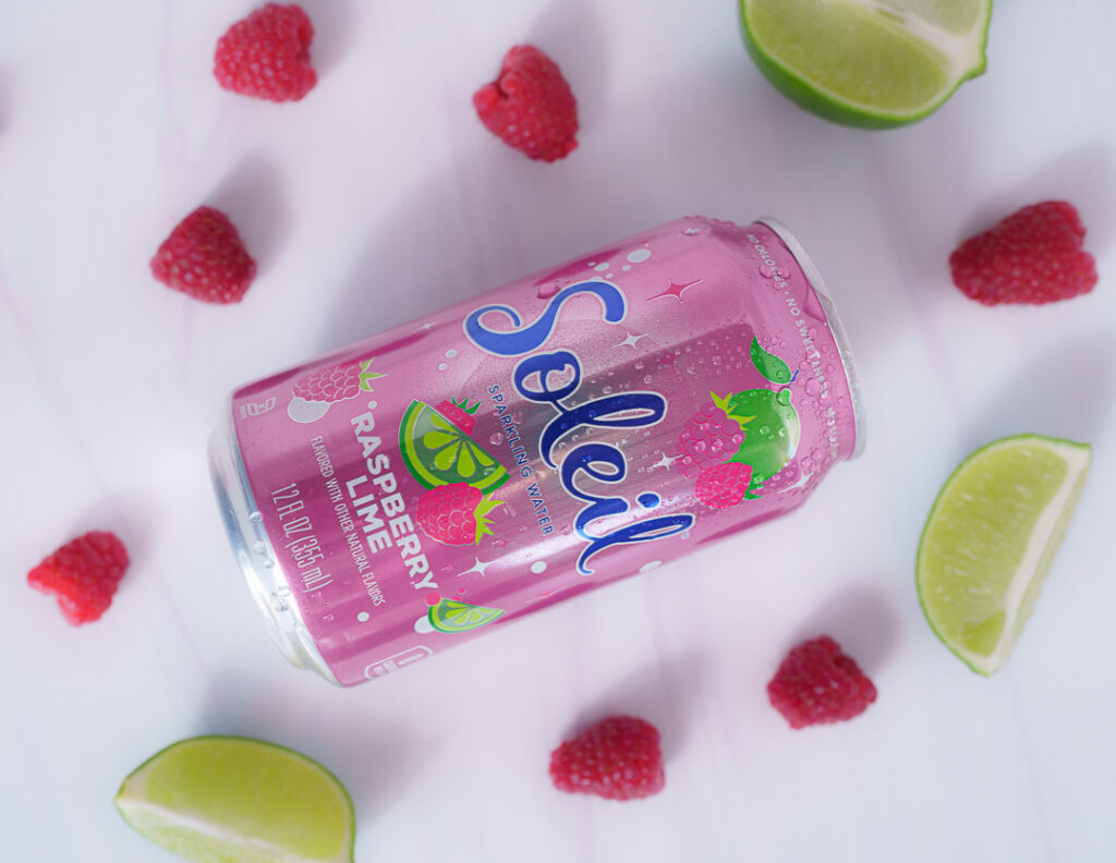 7 Ways a Brand Photoshoot Can Save You Time Creating Social Media Content 11 Pink can of Raspberry Lime Soleil laying on side with cut limes and raspberries on white background.