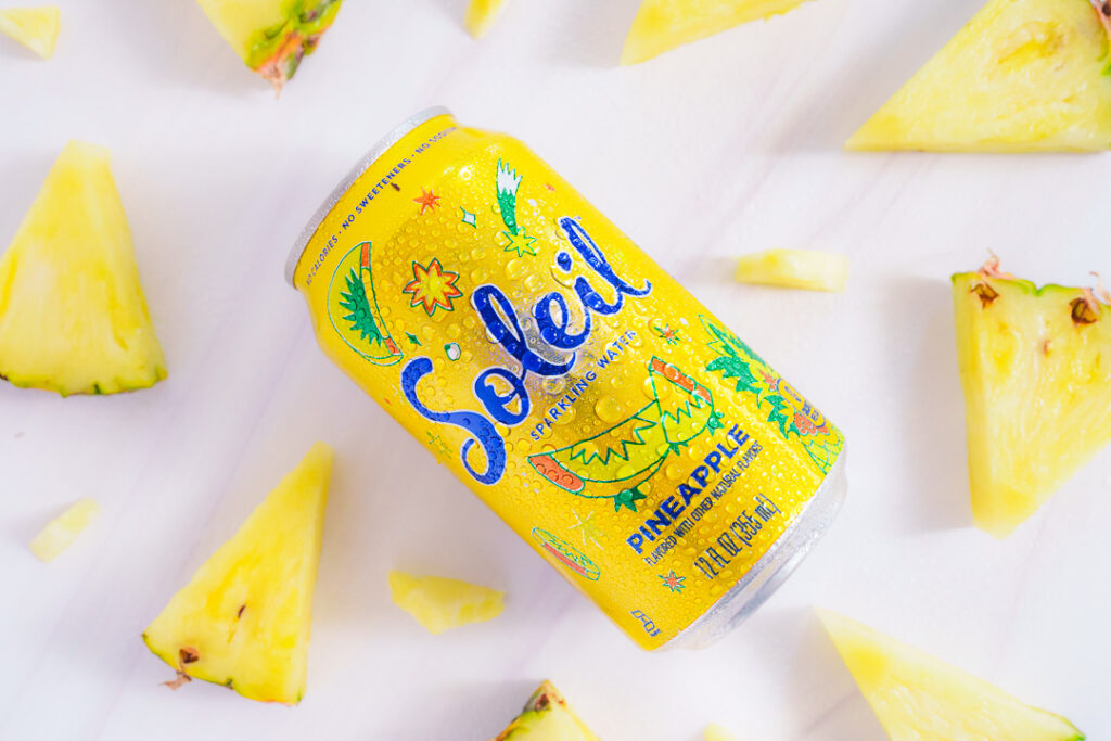 7 Ways a Brand Photoshoot Can Save You Time Creating Social Media Content 13 Yellow can of Pineapple Soleil laying on side with cut wedges of pineapple on a white background.
