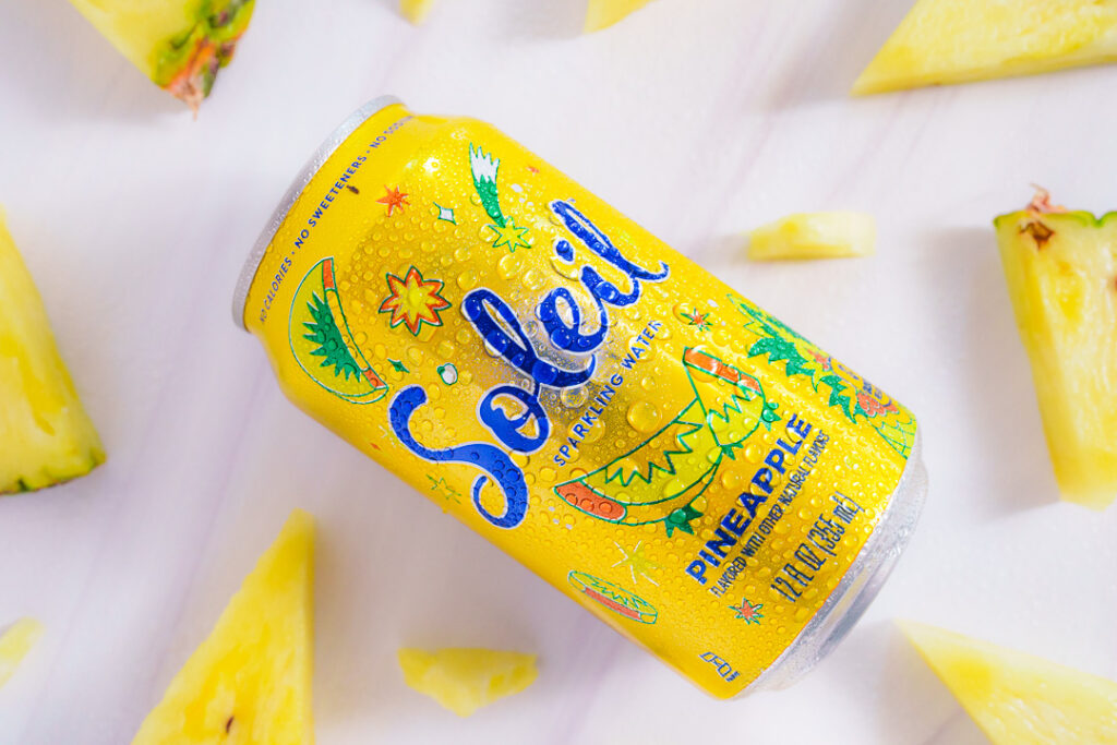 7 Ways a Brand Photoshoot Can Save You Time Creating Social Media Content 14 Yellow can of Pineapple Soleil laying on side with cut wedges of pineapple on a white background.