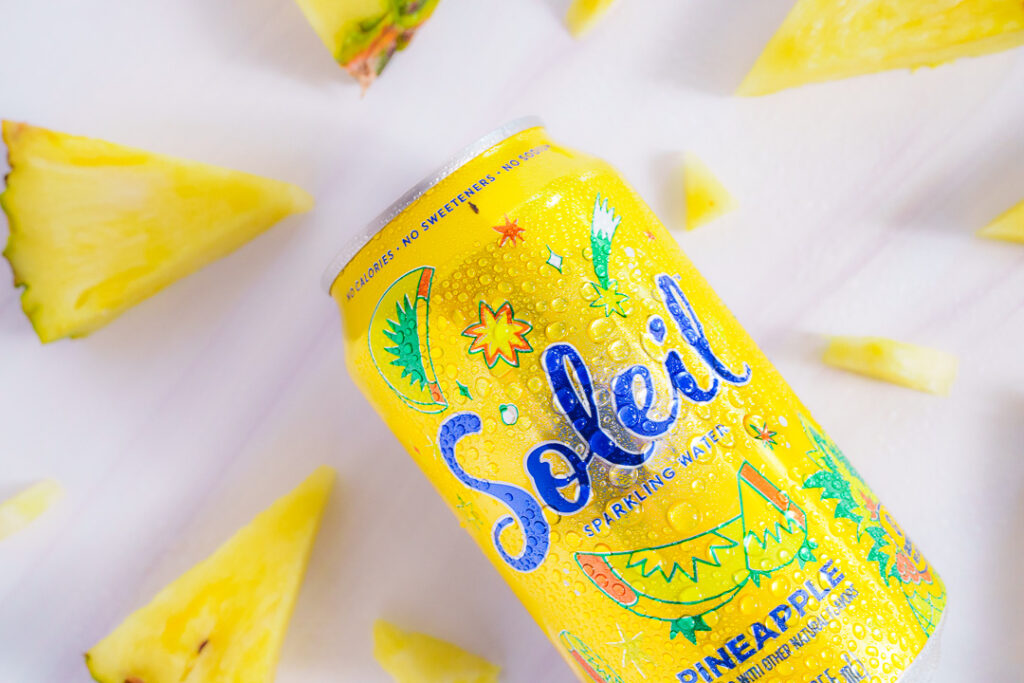 7 Ways a Brand Photoshoot Can Save You Time Creating Social Media Content 15 Yellow can of Pineapple Soleil laying on side with cut wedges of pineapple on a white background.