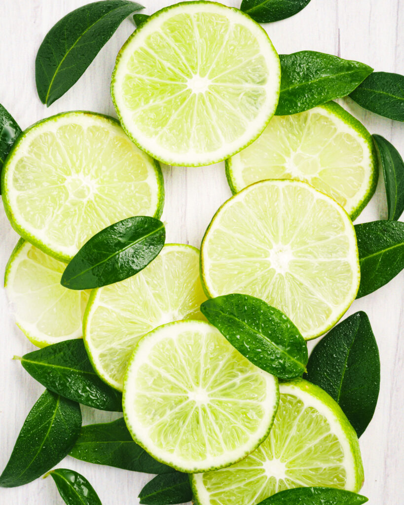 Still life photo of lime slices and leaves, showcasing vibrant greens contrast with a clean white background