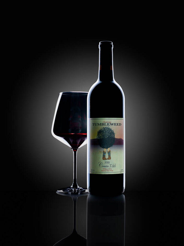 Bottle of Tumbleweed Cousin Idd wine with a poured glass of red wine paired with a dark and moody setting
