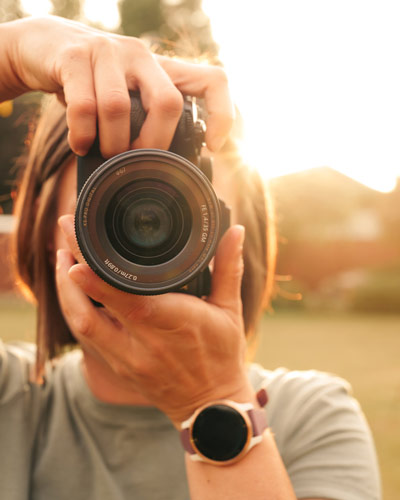 Debbie holds a camera in front of a golden sunset