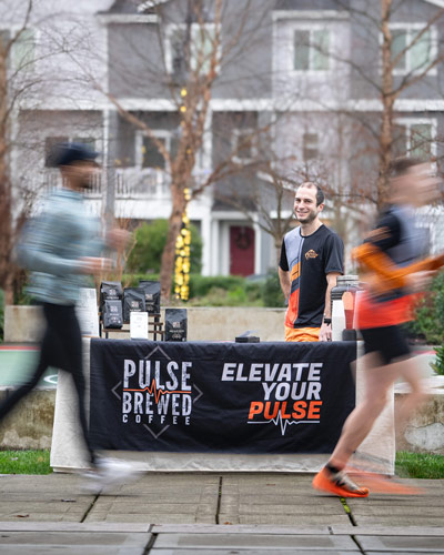 Runners run past the Pulse Brewed coffee coffee stand