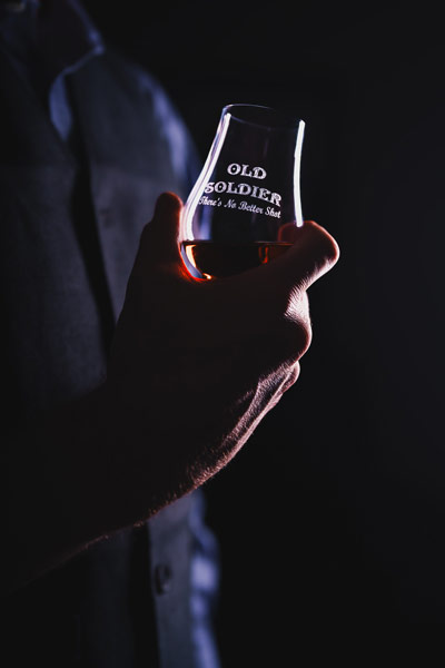 Hand holds Old Soldier glencairn whiskey glass in a dark, moody environment