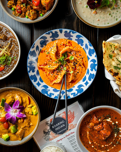 Bright plates of Roaring Indian curry sit atop a dark table.