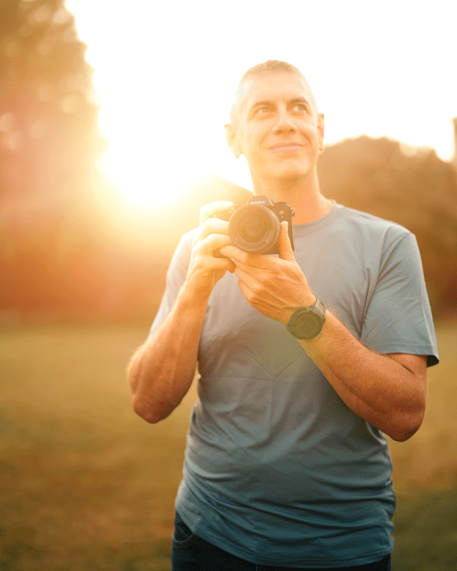 Jason Kudlo, Seattle brand photographer, holding camera in front of a golden sunset - Elemental Brand Photography