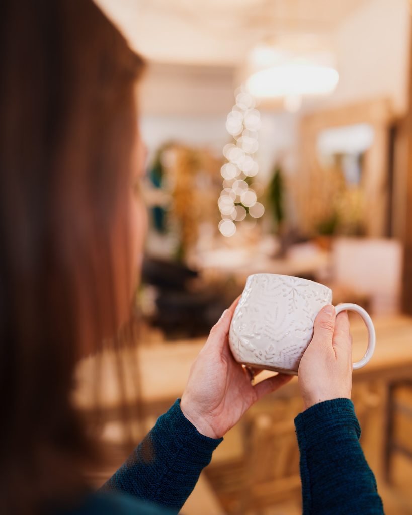 Holiday shopper holds a white mug with embossed snowflakes inside House & Hazel in Maple Valley, WA.