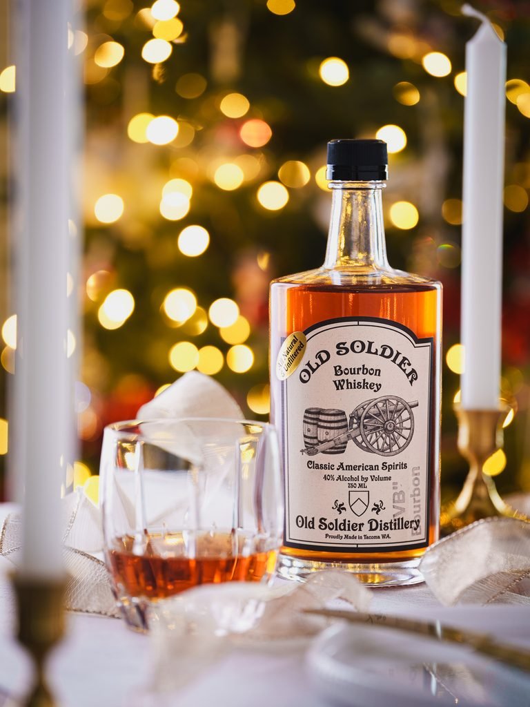 Bottle of Old Soldier Whiskey on a professionally styled table with a bright setting and holiday lights in the background.