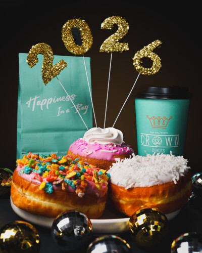 Showcasing branded products in a festive setting brings the brand to life. Connecting visuals to the New Year encourages engagement, strengthens brand recognition, and positions the products as part of meaningful moments. Crown donuts bag, coffee, donuts, and New Year's decor adorns a table in celebration of the 2026 New Year