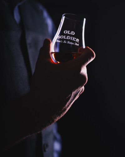 Dark, moody, intentional. Gentle edge light shapes the subject and glass, adding contrast, depth, and atmosphere that elevate the scene. Moodily lit Old Soldier glen cairn shows off the mood of the light while very subtly showing the caramel colors of the product.