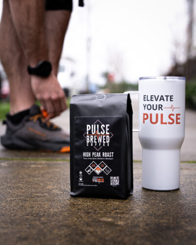 Showcasing a real-life moment with running shoes, coffee beans, and a branded mug emphasizes Pulse Brewed’s active lifestyle and community focus, making the brand relatable and memorable. Pulse Brewed High Peak Roast Coffee on the sidewalk with runner lacing shoes for run