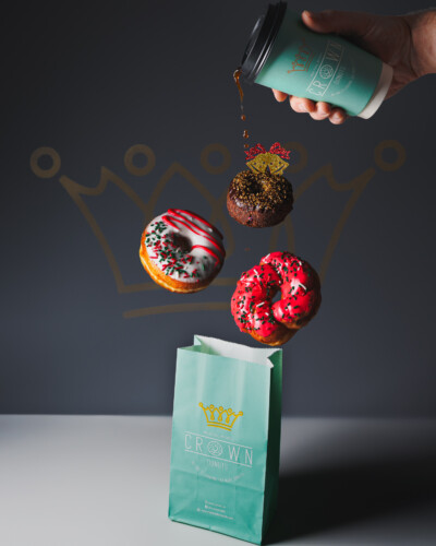 This image wasn’t captured in a single shot - it was built with intention. By adding light and stacking elements from 6 different shots in post, we created floating donuts and flowing coffee that highlight the product and add movement to the scene. Holiday donuts levitate over a bag from Crown donuts while a Crown donuts coffee cup spills it's coffee