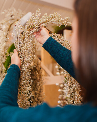Grasping the garland creates a natural, human moment, showing the product in action and helping viewers imagine it as part of their own holiday traditions. festive winter garland is picked up by a customer in House & Hazel