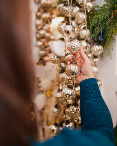 This perspective shows the product in action, creating a natural, relatable moment that draws viewers into the brand story. a hand holds the metallic ornaments strung through the garland at House & Hazel
