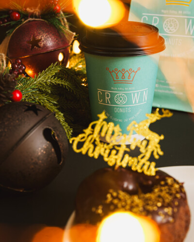A simple, tightly-focused holiday image ties the brand to seasonal traditions, helping build a connection with the viewer and elevate the brand during the holiday season. Christmas ornaments, a Merry Christmas donut, and a coffee cup sit on a table among additional holiday decor