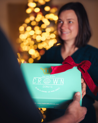 Even in a product-focused image, human connection matters. By including a person handing over the gift, we add warmth, relatability, and context - showing the brand in action and creating an emotional connection that a product alone can’t convey. A box of Crown donuts is gifted for the holiday season
