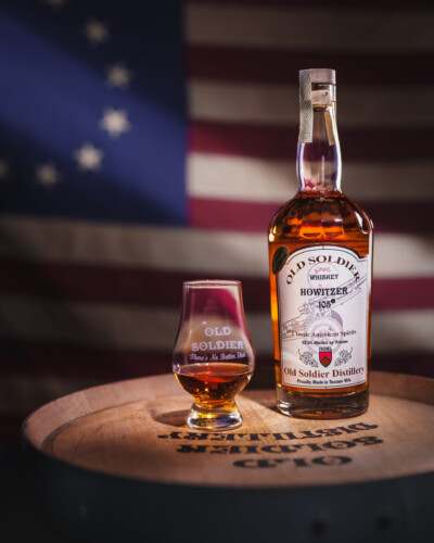 Depth, light, and attention to detail brought Old Soldier’s 105 Howitzer Bourbon to life. From the flag with a horizontal strip of light crossing it to the whiskey barrel and Glen Cairn glass, every element was intentionally lit to put the product front and center. Bottle of Old Soldier Distillery Howitzer 105 whiskey sits atop a whiskey barrel with a glen cairn glass, in front of a moodily lit Betsy Ross flag.
