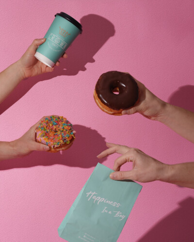 Bring out the fun with your product, using shadows to create that refreshing summer feel and welcome guests into your brand! Crown donuts and coffee are held in front of a pink background with summer shadows