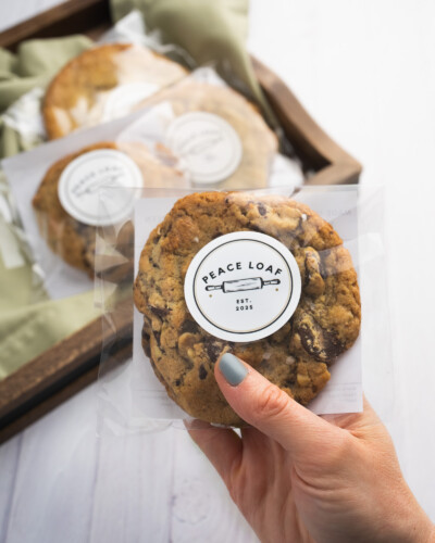 Holding the hero of the image away from additional items helps separate the hero - or main subject - from the scene while the brightness helps elevate the shot. Hand holds Peace Loaf cookie while a tray behind the hand holds a larger selection