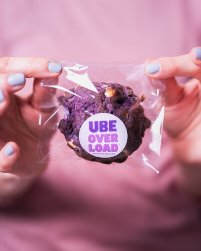 Sometimes simple is the best method - showcasing the product in a persons hands puts the viewer in the drivers seat Hand holds packaging containing an Ube Overload cookie