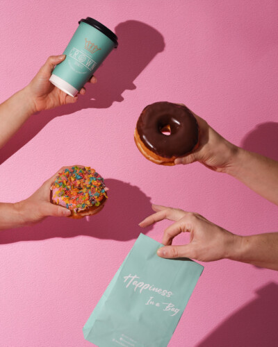 Bring out the fun with your product, using shadows to create that refreshing summer feel and welcome guests into your brand! Hands holding donuts and Crown Donut bag and coffee cup with hard shadows and a bright background