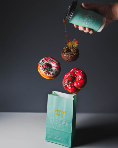 Seattle Product Photography for Crown Donuts in Maple Valley, WA. Fresh, small business holiday donuts falling out of a branded bag with drips of coffee flowing out of a cup - created as seasonal social media content and advertising content Seattle Product Photography - Crown Donuts Maple Valley, WA - advanced edit composite of falling coffee & donuts above open crown donut bag - Elemental Brand Photography