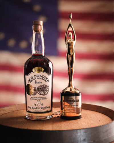 Seattle Product Photography for Old Soldier Distillery in Tacoma, WA. John Barley Gold award staged next to the award winning Santos Bourbon with a bright natural night and soft reflections in front of the Betsy Ross American flag - created for social media and marketing advertising Seattle Product Photography - John Barley Gold Award winner with Santos bourbon - Old Soldier Distillery - Tacoma, WA - Elemental Brand Photography