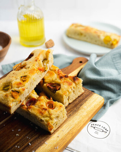 Seattle product photography for Peace Loaf in Maple Valley, WA. A focaccia loaf rests on a cutting board beside a bottle of olive oil and a sliced piece - relatable in-home lifestyle imagery for a Pacific Northwest naturally leavened artisan bakery. Seattle Product Photography - Peace Loaf Focaccia on Cutting Board with Olive Oil in In-Home Lifestyle Setting - Pacific Northwest Artisan Bakery - Peace Loaf - Maple Valley, WA - Elemental Brand Photography