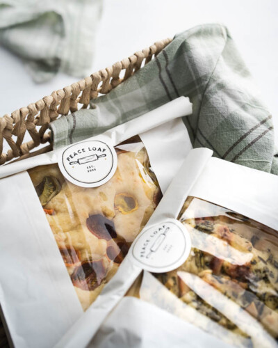 Seattle product photography for Peace Loaf in Maple Valley, WA. Two naturally leavened focaccia loaves rest in a basket with the Peace Loaf label visible - bright, clean product imagery for a Pacific Northwest values-driven artisan bakery. Seattle Product Photography - Peace Loaf Focaccia Bread Loaves in Basket with Branded Label - Naturally Leavened Artisan Bakery - Peace Loaf - Maple Valley, WA - Elemental Brand Photography