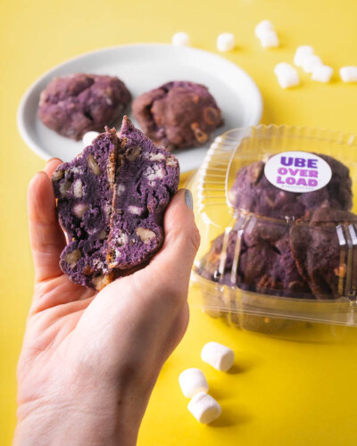Seattle product photography for Ube Overload. A hand holds an ube overload cookie split in half, revealing the marshmallow, white chocolate, and nut-studded interior - ingredient storytelling product photography for a Pacific Northwest artisan dessert brand. Seattle Product Photography - Hand Holding Ube Overload Cookie Split in Half Revealing Marshmallow White Chocolate and Nuts - Ube Overload - Maple Valley, WA - Elemental Brand Photography