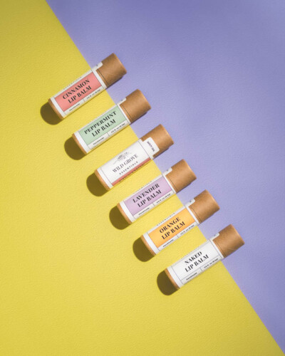 Seattle product photography for Wild Grove Essentials. Five natural lip balm flavors arranged diagonally on a vibrant purple and yellow gradient - clean, product-forward social media content for a nature-inspired Pacific Northwest wellness brand. Seattle Product Photography - Wild Grove Essentials Five-Flavor Lip Balm Collection on Bold Gradient Background - Pacific Northwest Wellness Brand - Maple Valley - Elemental Brand Photography