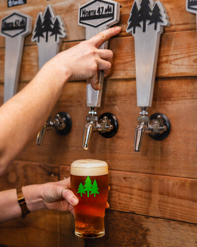 Seattle restaurant photography for North 47 Brewing Co. in Tacoma. Desaturated edges draw the eye from the branded glass up to the IPA tap - intentional composition that keeps the brand identity front and center. Seattle Restaurant Photography - North 47 IPA Tap with Branded Glass in Foreground - Desaturated Edges Guide Eye to Logo - Tacoma - Elemental Brand Photography