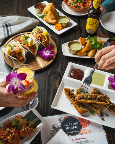 Seattle Restaurant Photography for Roaring Indian Plates & Pours in Maple Valley, WA. Multiple appetizers spread through the scene showcasing the variety or authentic, gourmet indian starters available with soft, even lighting and a human element - created for social media content to share the experience and quality at the local small-business restaurant. Seattle Restaurant Photography - Roaring Indian Plates & Pours - Human element and appetizers - Maple Valley, WA - Elemental Brand Photography